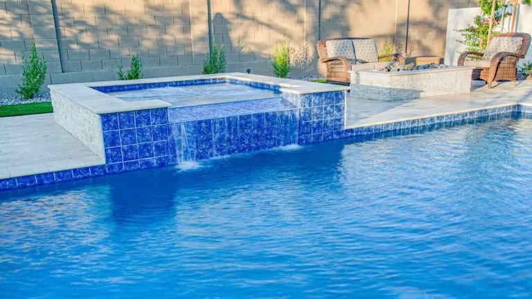 A shimmering azure pool and exquisite mosaic-tiled spa with a cascading tranquil waterfall in a refined backyard retreat
