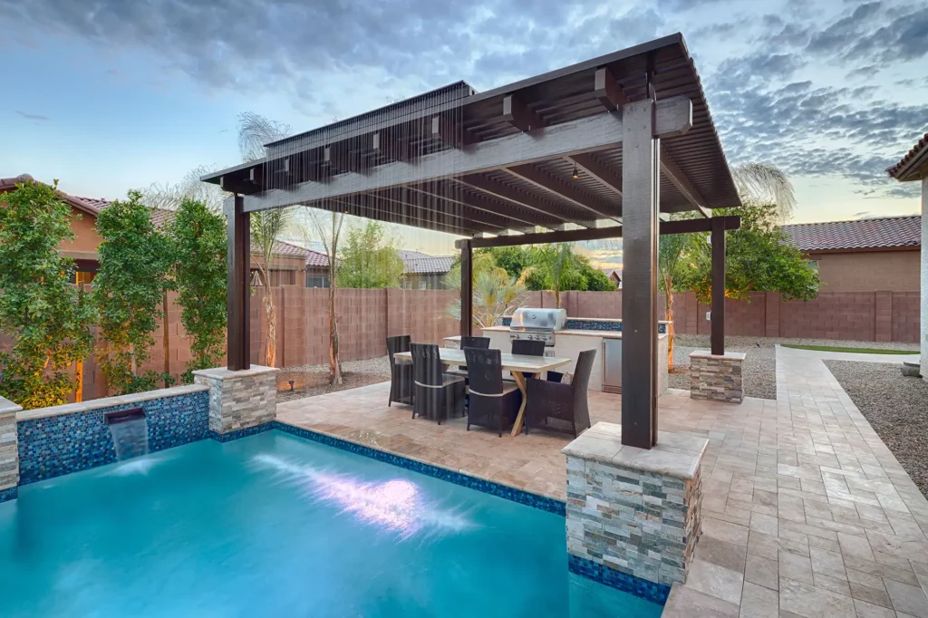 A lavish and serene poolside patio in Arizona, showcasing a glittering pool, exquisite outdoor kitchen, and refined dining area beneath an elegant architectural pergola