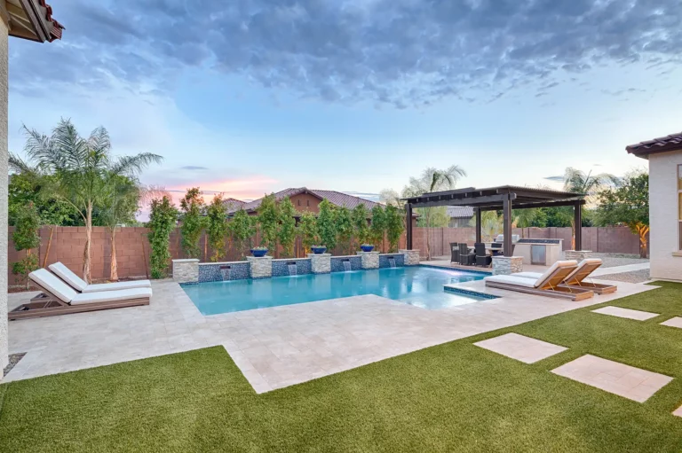 A sumptuous backyard oasis, featuring a serene pool with cascading waterfalls, elegant chaise lounges, and a refined outdoor living area under a twilight sky