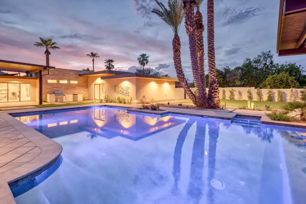 Exquisite, tranquil poolside retreat: radiant blue pool reflects sophisticated modern home and palm trees under twilight