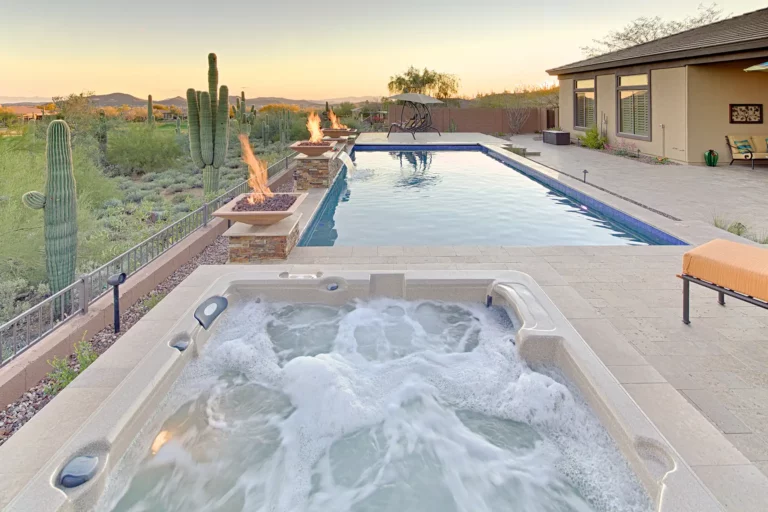 An opulent desert escape featuring a bubbling spa and a tranquil pool, framed by elegant fire features and majestic cacti