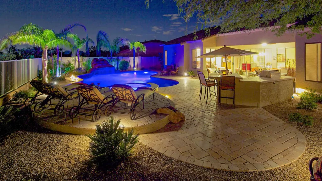 Sumptuous, enchanting backyard oasis at night, with serene azure pool water, elegant patio, and ambient lighting