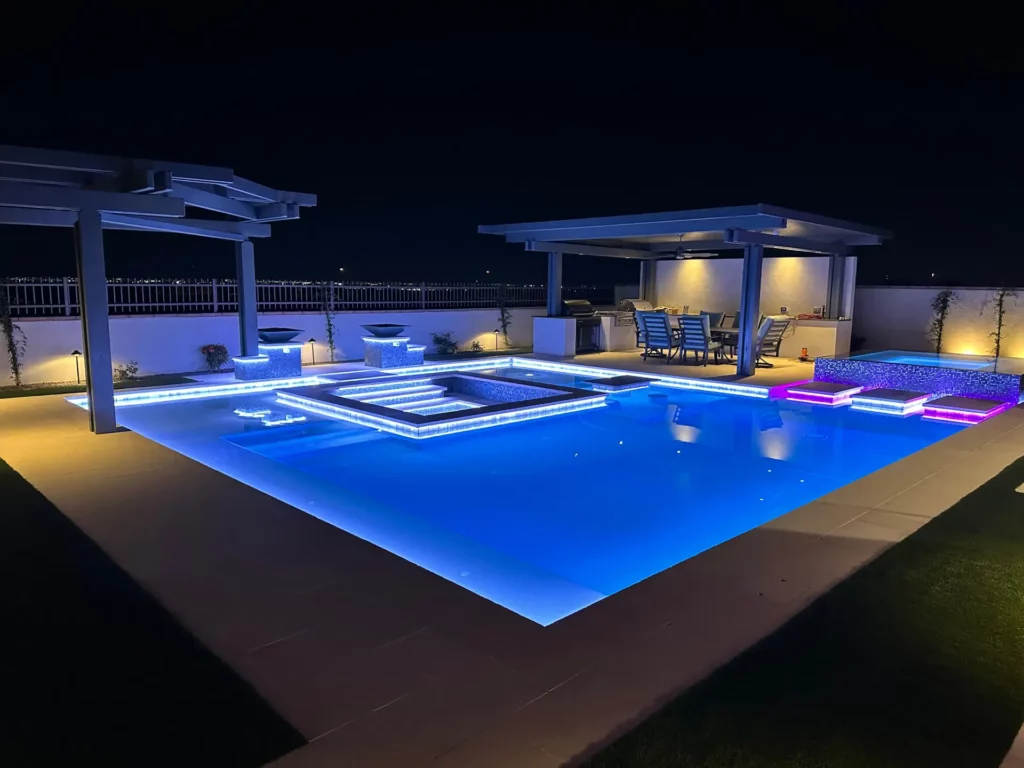 Exquisite nocturnal poolside retreat with shimmering azure water, a lavish raised spa, and an elegant outdoor kitchen area