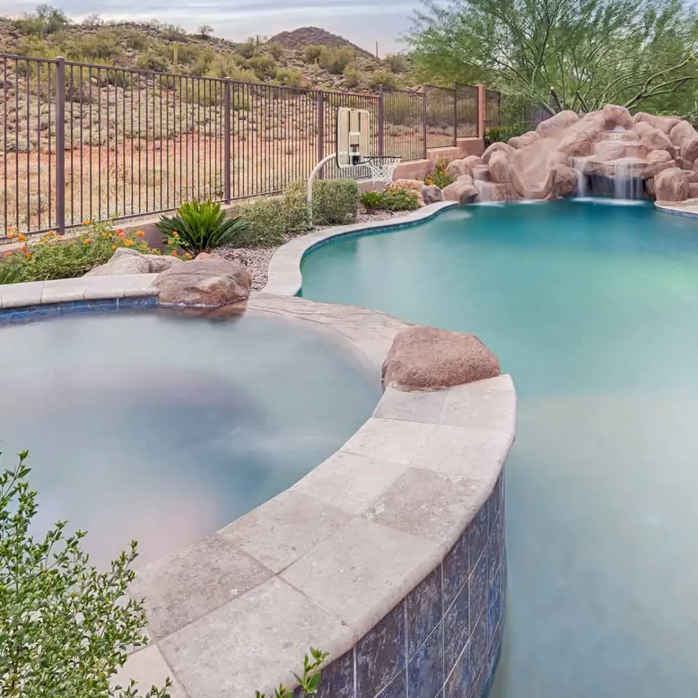 Serene desert oasis: a lavish pool and spa with an exquisite rock waterfall feature, set against arid hills