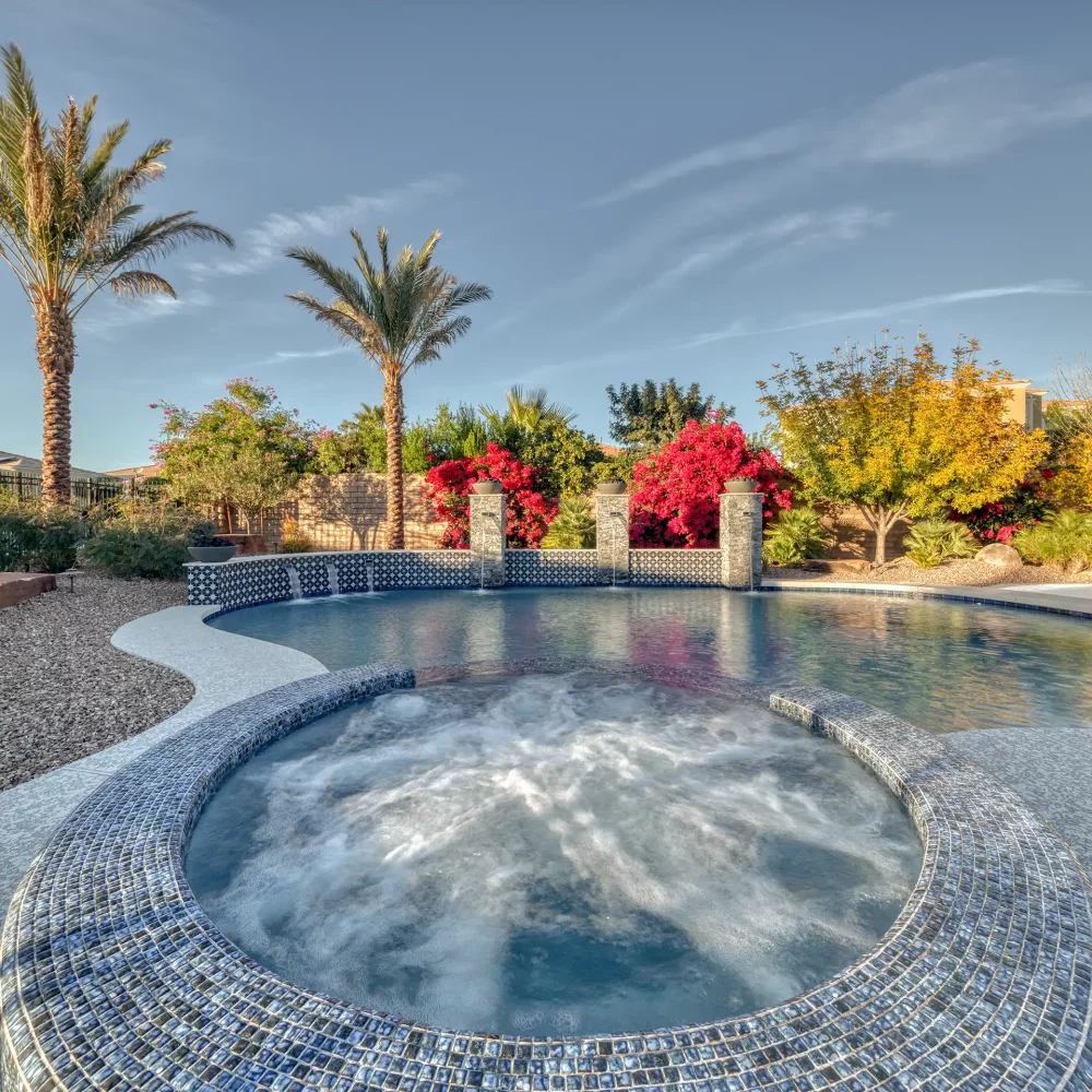 Exquisite poolside retreat featuring tranquil waterfalls, ornate tile, and captivating fire bowls, creating a luxurious and serene atmosphere